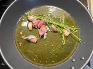 Bild zeigt eine Bratpfanne in der Knoblauch, Chili und Petersilienstängel braten.